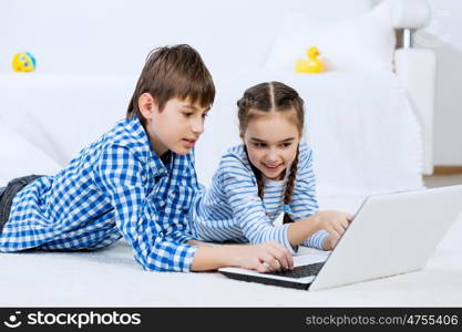 Cute kids using devices . Boy and girl using laptop while lying on floor