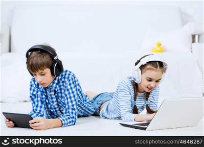 Cute kids using devices . Boy and girl using tablet and laptop while lying on floor