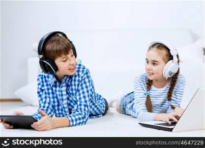 Cute kids using devices . Boy and girl using tablet and laptop while lying on floor