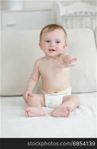 Cute laughing baby boy in diapers sitting on bed