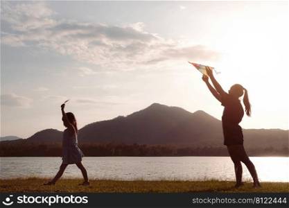 Cute litt≤girl flying a kite whi≤running on a meadow by the lake at sunset with her mother. Hea<hy∑mer activity forχldren. Funny time with family.