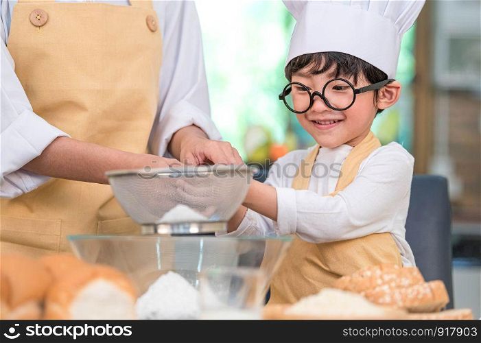 Cute little Asian boy and beautiful mother sifting dough flour with sifter sieve colander in home kitchen on table for prepare to baking bakery and cake. Thai kids playing with flour as chef funny