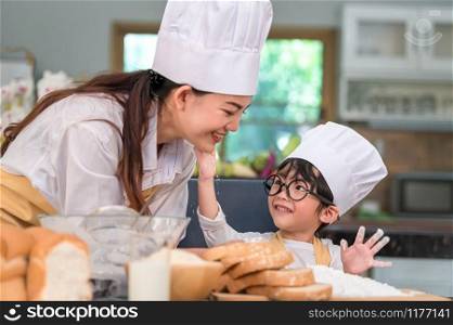 Cute little Asian boy painting beautiful woman face with dough flour. Chef team playing and baking bakery in kitchen funny. Homemade food and bread. Education and people lifestyles learning concept