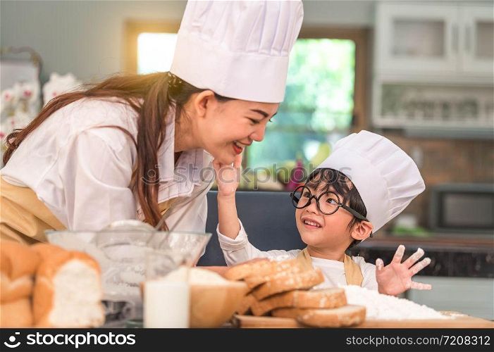 Cute little Asian boy painting beautiful woman face with dough flour. Chef team playing and baking bakery in home kitchen funny. Homemade food and bread. Education teamwork and learning concept.
