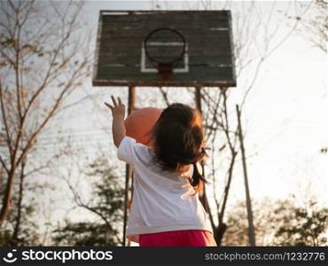 Cute little Asian child playing basketball on playground on summer day. Healthy outdoor sport for young child.