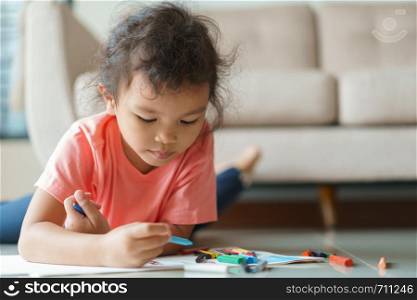 Cute little asian girl drawing homework and writing with color Wax crayons on paper in her home