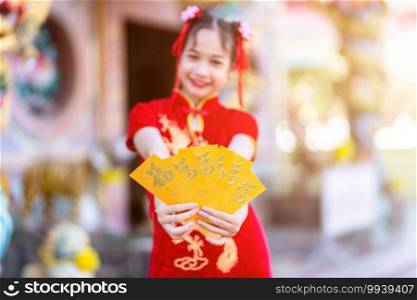 Cute little Asian girl wearing red traditional Chinese cheongsam decoration focus show holding yellow envelopes in hand for Chinese New Year Festival at Chinese shrine