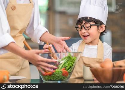 Cute little Asian happy boy interested in cooking with mother funny in home kitchen. People lifestyles and Family. Homemade food and ingredients concept. Two Thai people making ketogenic diet salad