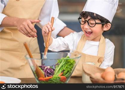 Cute little Asian happy boy interested in cooking with mother funny in home kitchen. People lifestyles and Family. Homemade food and ingredients concept. Two Thai people making ketogenic diet salad