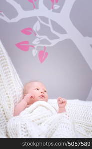 Cute little baby lying down in bedroom, charming infant relaxing at home wrapped in white knitted blanket, happy and healthy childhood concept