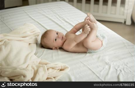 Cute little baby lying on bed and holding feet