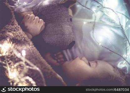 Cute little baby sleeping at home in his bed with his best friend, soft toy dog, vintage style photo with glowing lights, happy toddler dreaming. Cute little baby sleeping at home