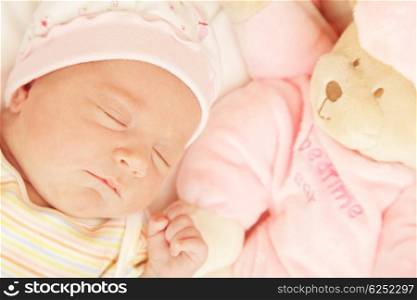 Cute little baby sleeping in pink pajama with teddy bear toy