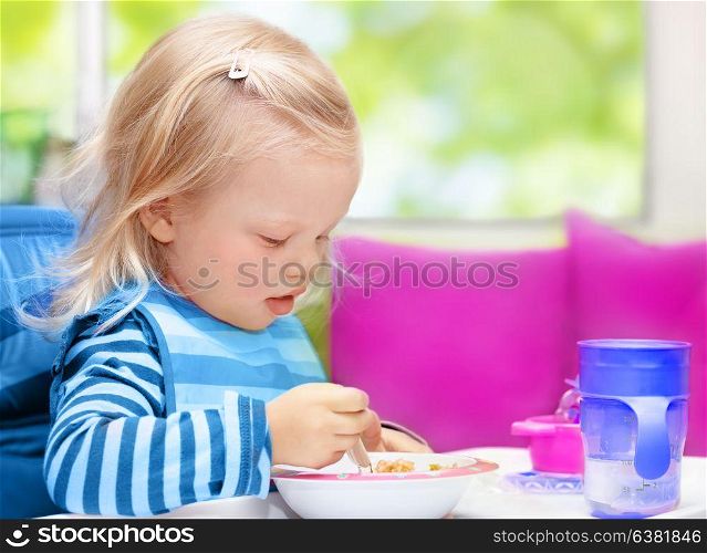 Cute little blond baby girl sitting on the kitchen at home and having breakfast, healthy child&rsquo;s nutrition, happy carefree childhood