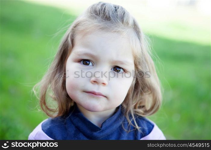 Cute little blonde girl looking at camera with grass of background