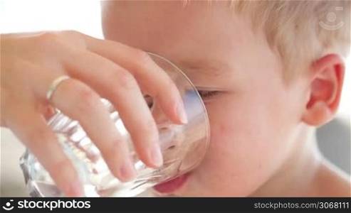 Cute little boy drinkng a glass of fresh water being held by his mother as he quenches his thirst