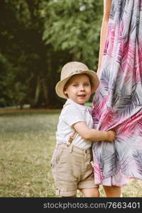 Cute, little boy holding a mother’s leg