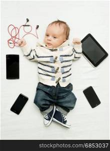 Cute little boy lying on bed with digital tablets and smartphones