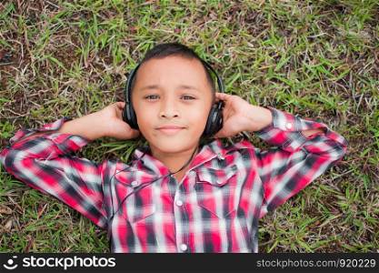 cute little boy lying on grass with headphone for listening in the park, his face feel like happy with sunshine. subject is blurry.