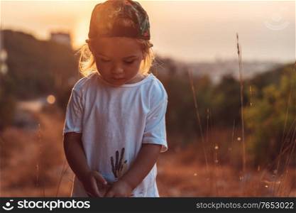 Cute little boy on the walk, sweet child with pleasure spending time outdoors, enjoying warm summer evening and beautiful sunset