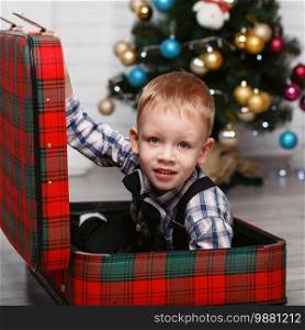 Cute Little boy playing hiding in a red plaid suitcase in the interior with Christmas decorations