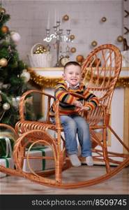 cute little boy sitting in rocking chair near christmas tree.. cute little boy sitting in rocking chair near christmas tree