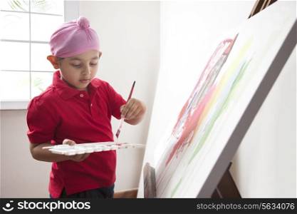 Cute little boy standing in front of canvas with a paintbrush