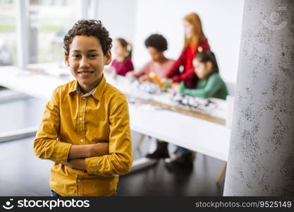 Cute little boy standing in front of  group of kids programming electric toys and robots at robotics classroom