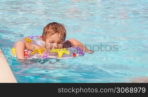 Cute little boy swimming with inflatable ring near the board of the pool