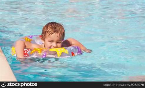 Cute little boy swimming with inflatable ring near the board of the pool