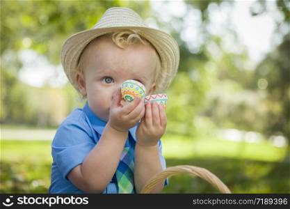 Cute Little Boy Wearing Hat Enjoying His Easter Eggs on Picnic Blanket Outside in the Park.
