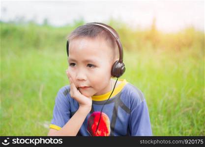 cute little boy with headphone for listening in the park, his face feel like happy with sunshine. subject is blurry.
