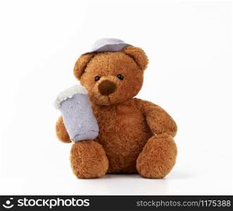 cute little brown teddy bear holds a felt mug with foam and is dressed in a gray hat, toy is sitting on a white background