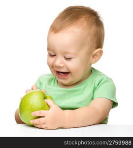 Cute little child is eating green apple while sitting at table, isolated over white