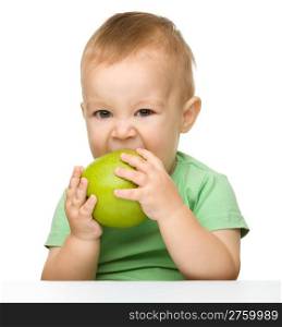 Cute little child is eating green apple while sitting at table, isolated over white
