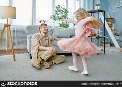 Cute little daughter princess with magic wand and father wearing costumes having fun at home. Cute little daughter with magic wand and father kidding at home