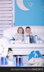 cute little girl and boy with gift boxes sitting on a white sofa. celebrating Christmas and New Year.. cute little girl and boy with gift boxes sitting on a white sofa. celebrating Christmas and New Year