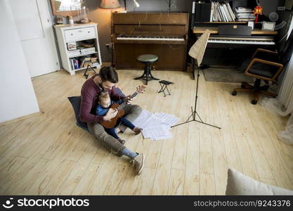 Cute little girl and her handsome father are playing guitar and smiling while sitting  at home