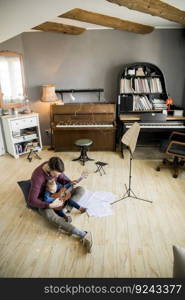 Cute little girl and her handsome father are playing guitar and smiling while sitting  at home