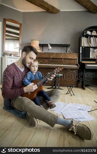 Cute little girl and her handsome father are playing guitar and smiling while sitting  at home