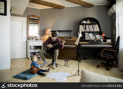 Cute little girl and her handsome father are playing guitar and smiling while sitting  at home