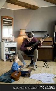 Cute little girl and her handsome father are playing guitar and smiling while sitting  at home