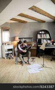 Cute little girl and her handsome father are playing guitar and smiling while sitting  at home