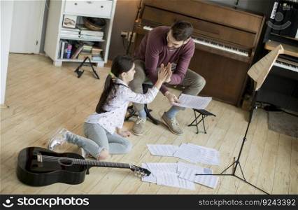 Cute little girl and her handsome father are playing guitar and smiling while sitting  at home