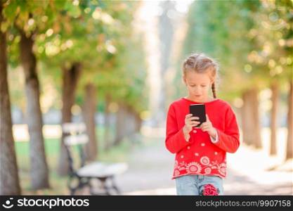 Cute little girl at beautiful warm spring day outdoors with smartphone in hands. Adorable little girl at beautiful autumn day outdoors