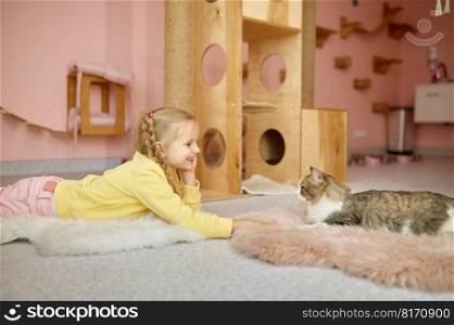 Cute little girl child looking how cat crawl out of cage spending time at pet zoo or animal shelter. Little girl child looking how cat crawl out of cage spending time at pet zoo