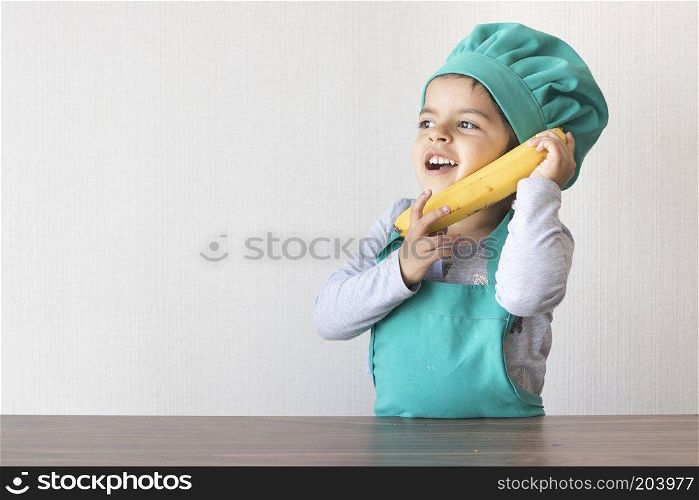 Cute little girl cook playing with a banana, as if it were a phone