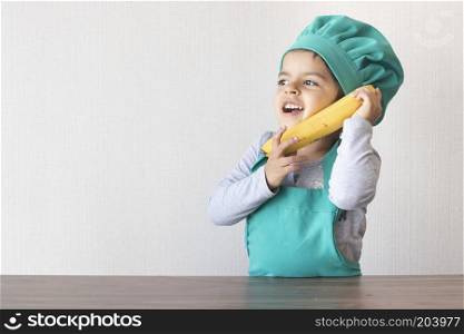Cute little girl cook playing with a banana, as if it were a phone