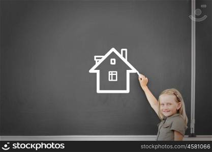Cute little girl drawing house on blackboard. School girl at blackboard