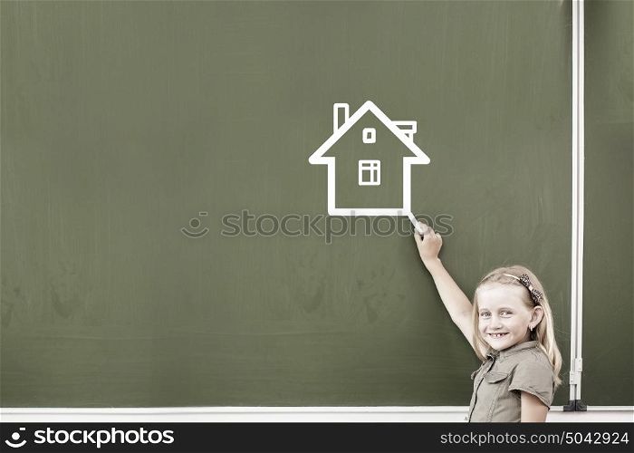 Cute little girl drawing house on blackboard. School girl at blackboard